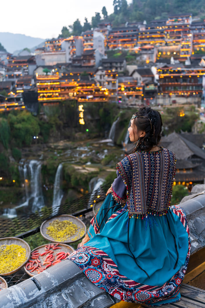 Mujer oservando la ciudad de lijiang con traje típico de la zona y en el fondo cascadas